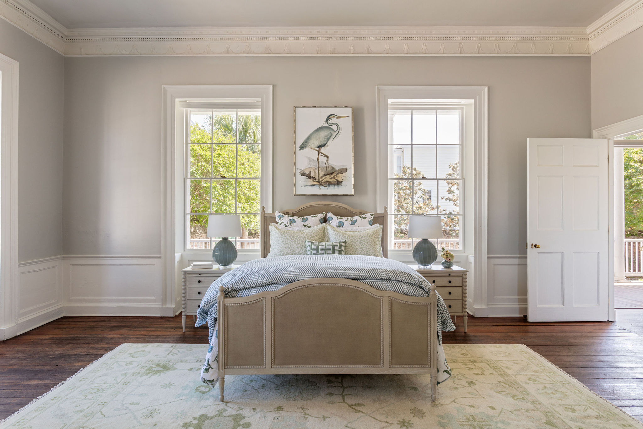 lifestyle image of a bed made up in block print bedding, bobbin trim bed and nightstand, teal lamps, and framed heron picture