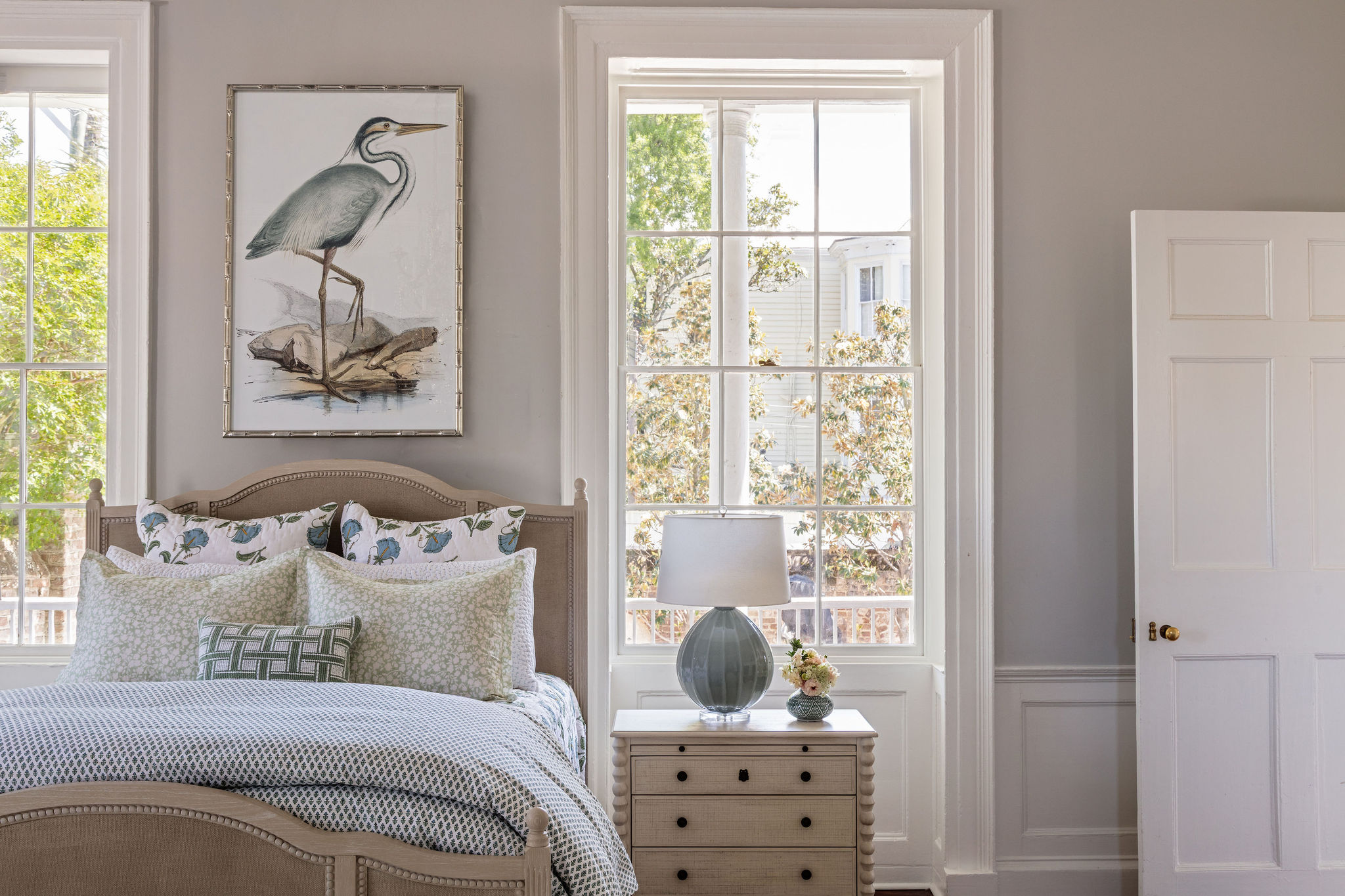 lifestyle image of a bed made up in block print bedding, bobbin trim bed and nightstand, teal lamp, and framed heron picture