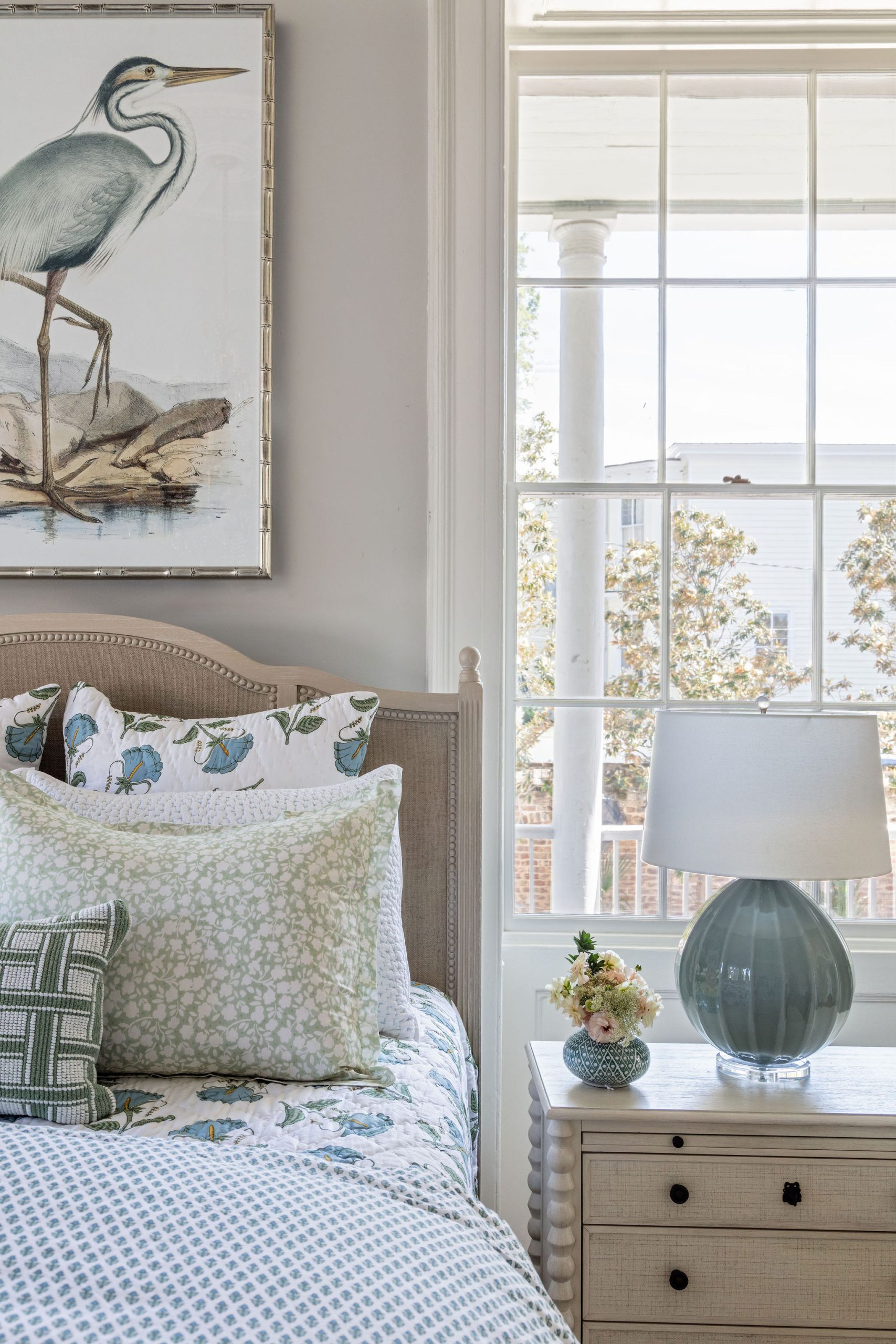 lifestyle image of a bed made up in block print bedding, bobbin trim bed and nightstand, teal lamp, and framed heron picture