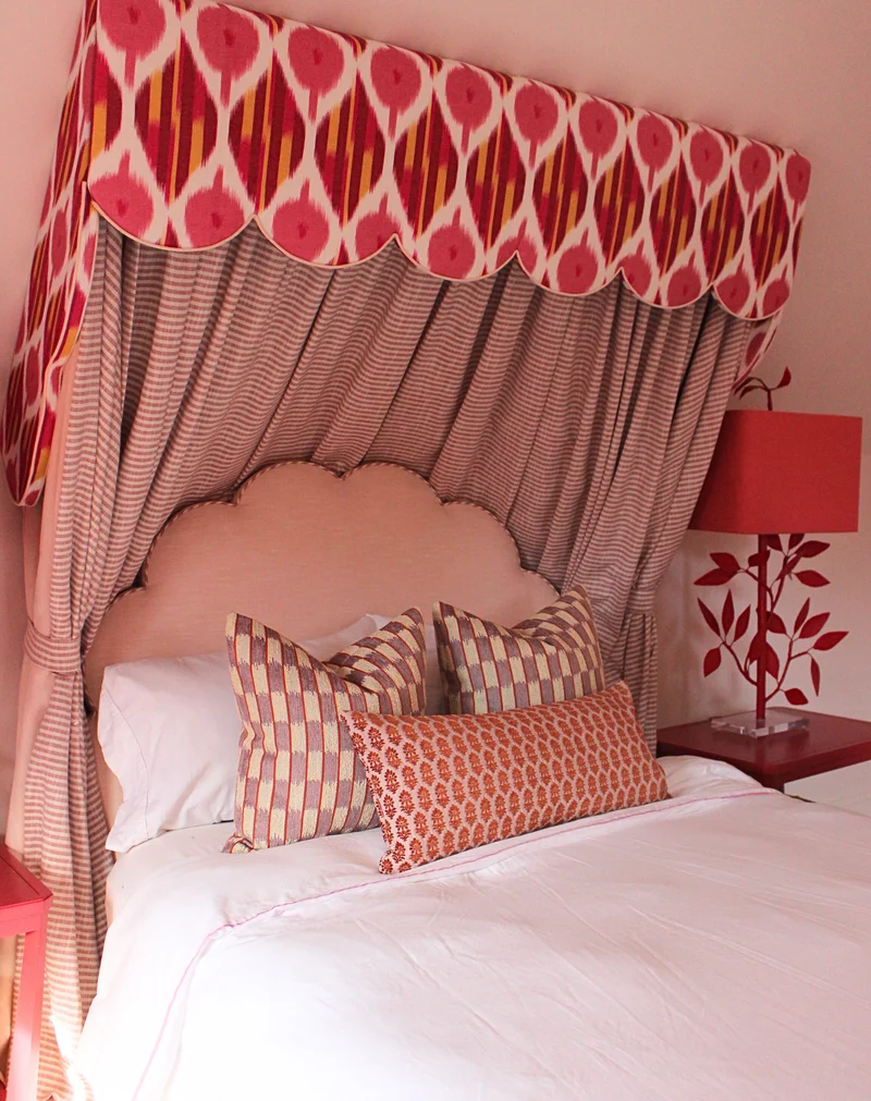 lifestyle image of a bed made up with pink, red, and purple decorative pillows