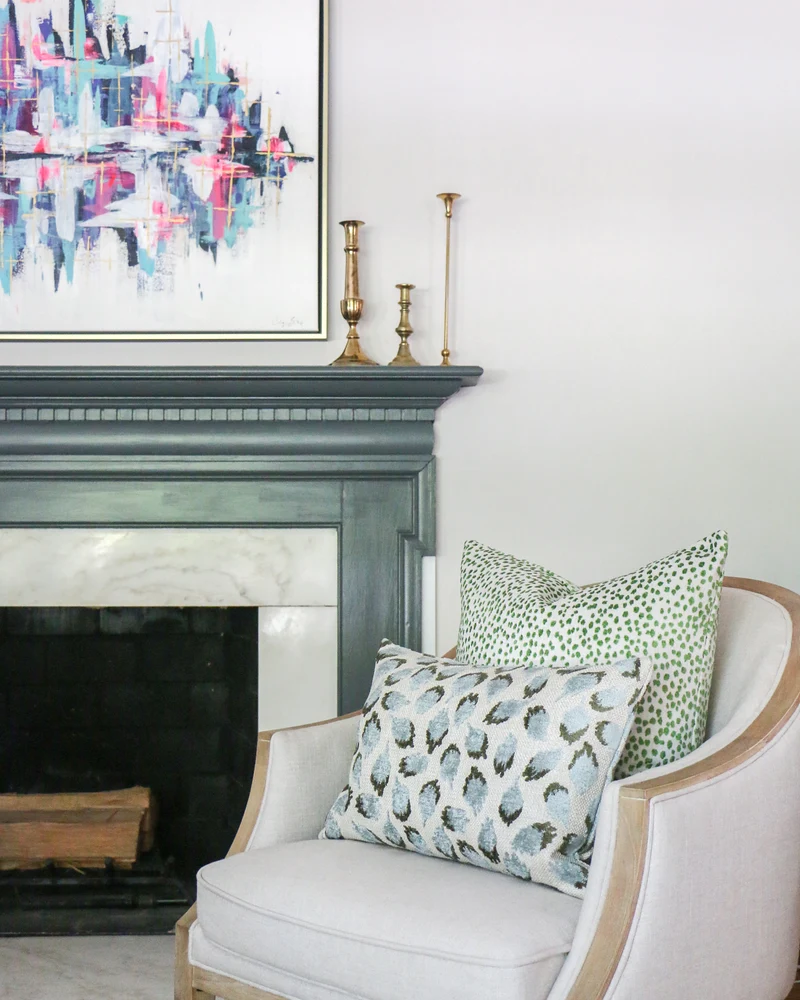 neutral chair beside a fireplace with two cut velvet decorative pillows in green and blue
