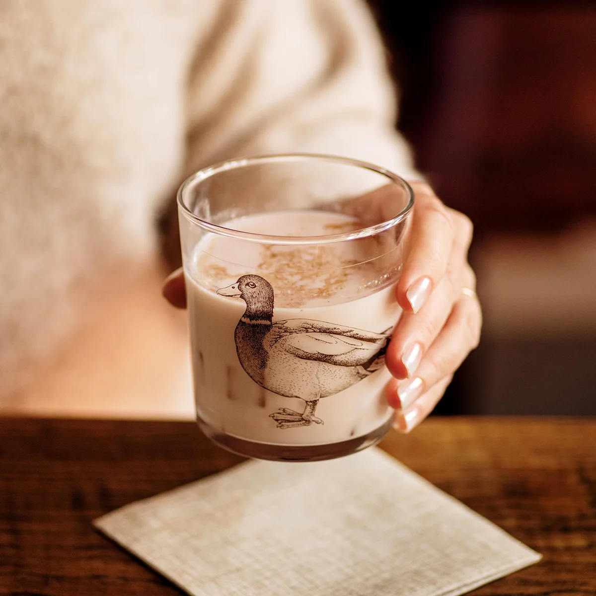 woman's hand holding a glass tumbler with a mallard print