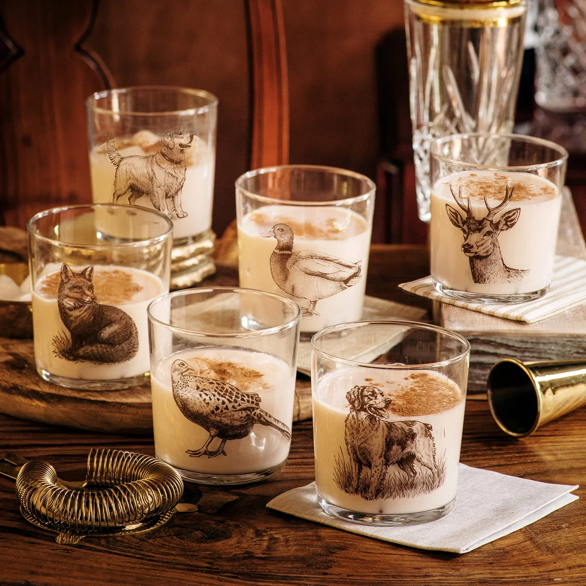 lifestyle image of six glass tumblers with wildlife animal prints shown with holiday cocktails and barware
