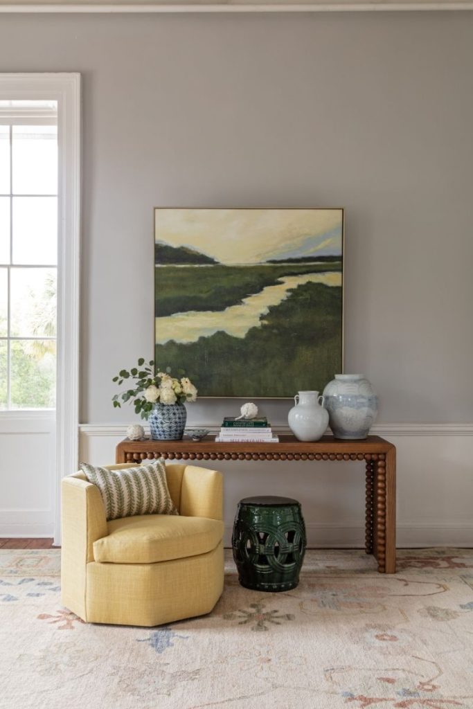 An accent chair in a living room near a console table topped with Charleston home decor and coastal art