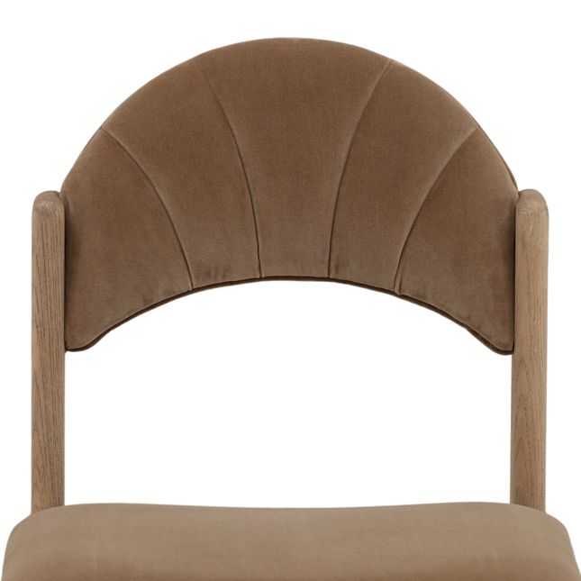 detail of a dining chair with a wood frame, light brown velvet seat and back, and curved scalloped backrest