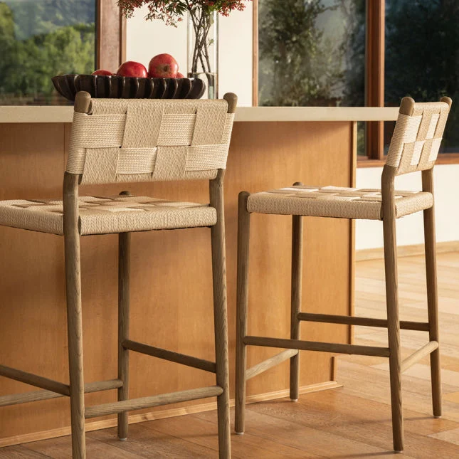 lifestyle image of two counter stools with wood frames and woven paper cord seats and backs in a neutral, modern kitchen