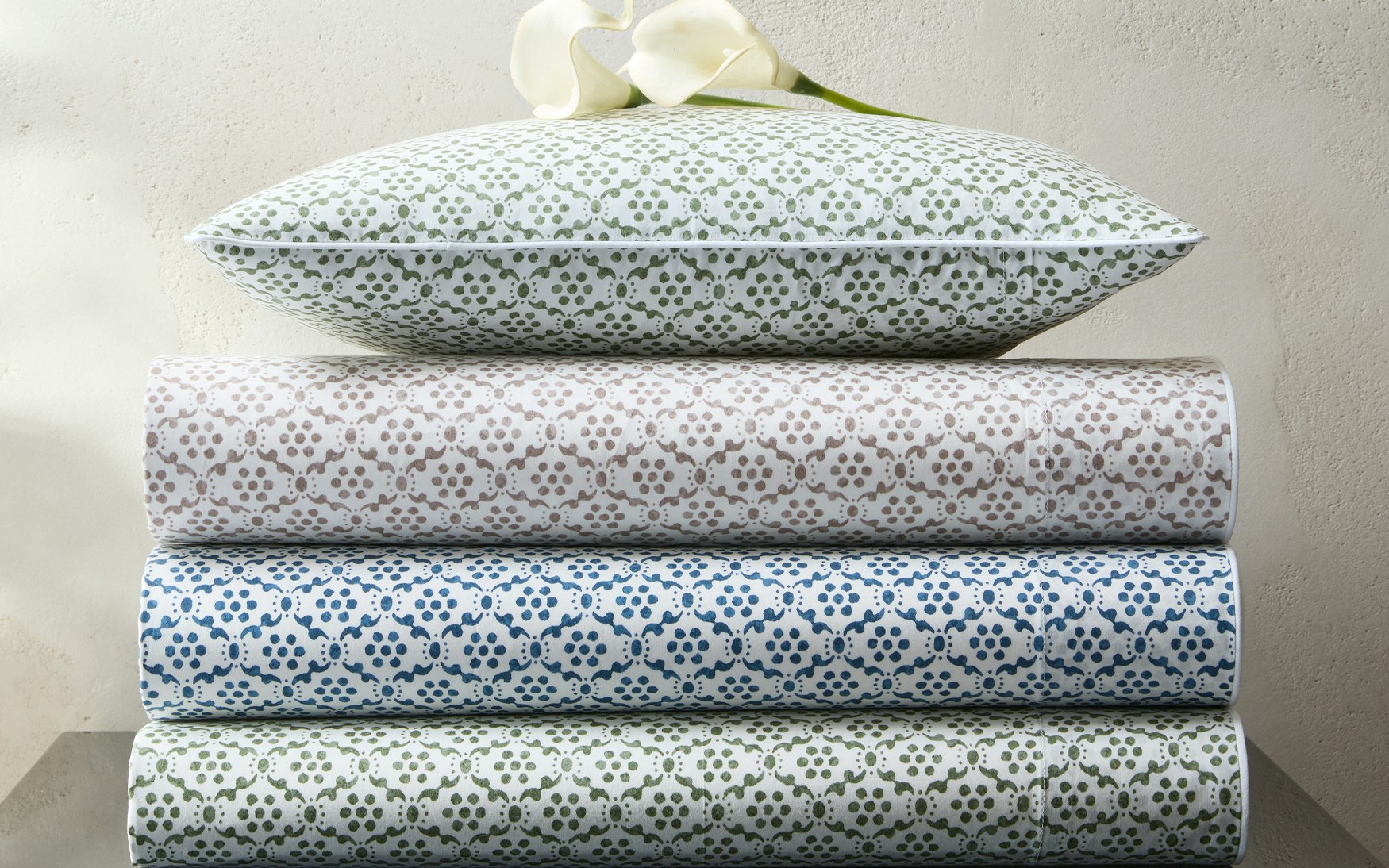 stack of folded bedding with small scale block print in green, taupe, and indigo
