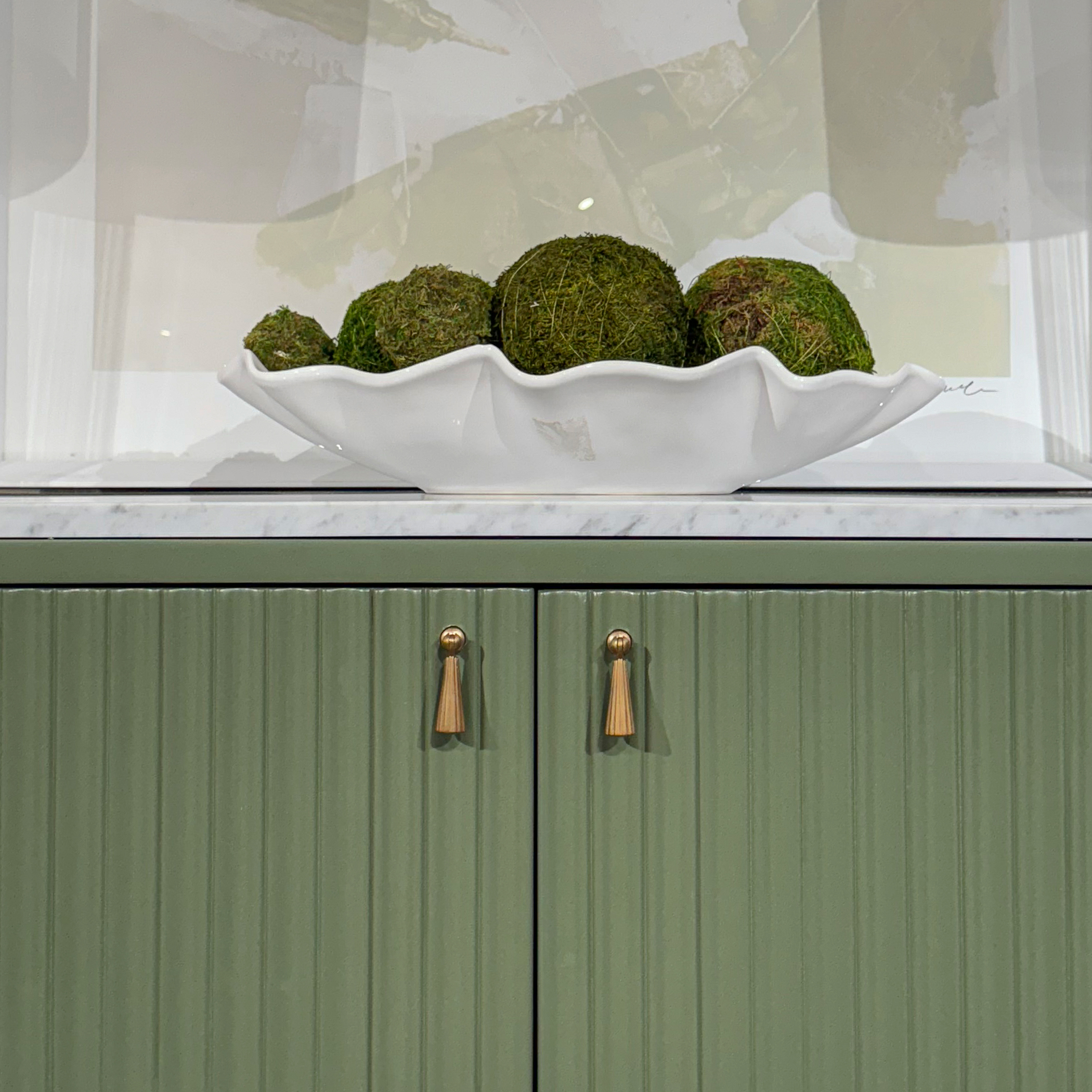 detail of a green console with a marble top, pleated doors, and brass tassel pulls shown with a decorative bowl of greenery on top
