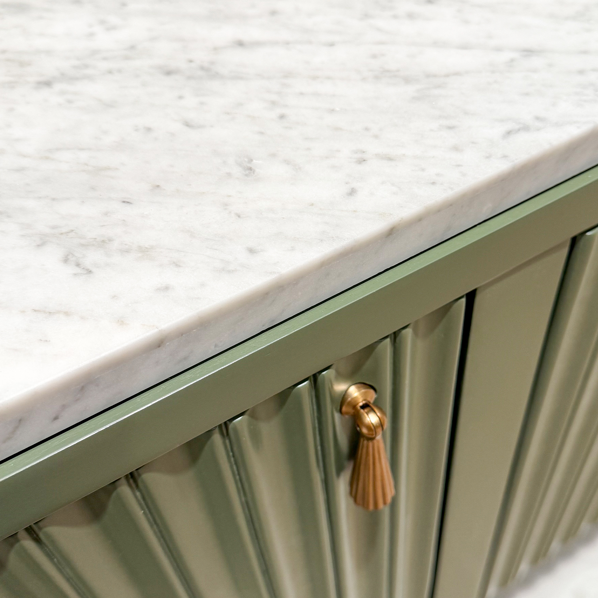 detail of a green console with a marble top, pleated doors, and brass tassel pulls
