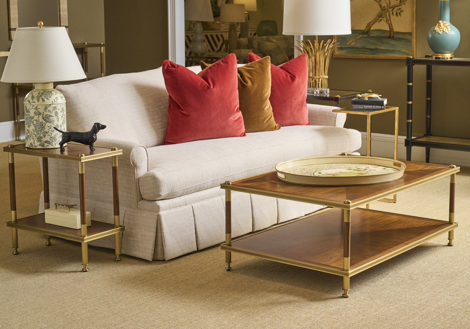 living room with a neutral sofa, red pillows, and rich wood tables with brass detail